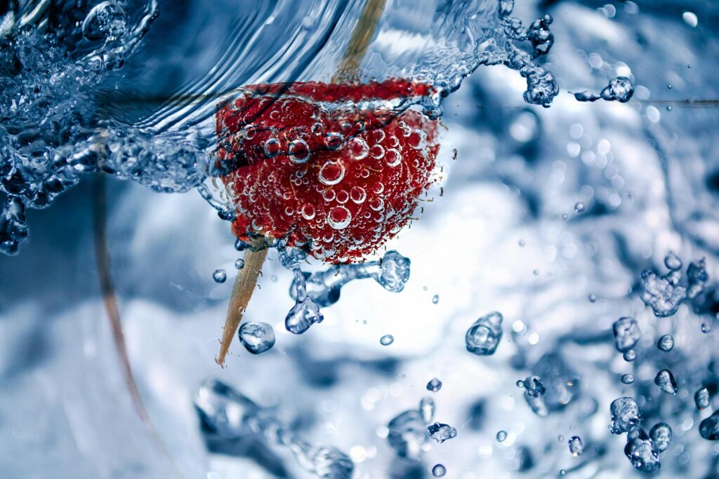 Close-up of a raspberry submerged in water, with bubbles and splash effect.